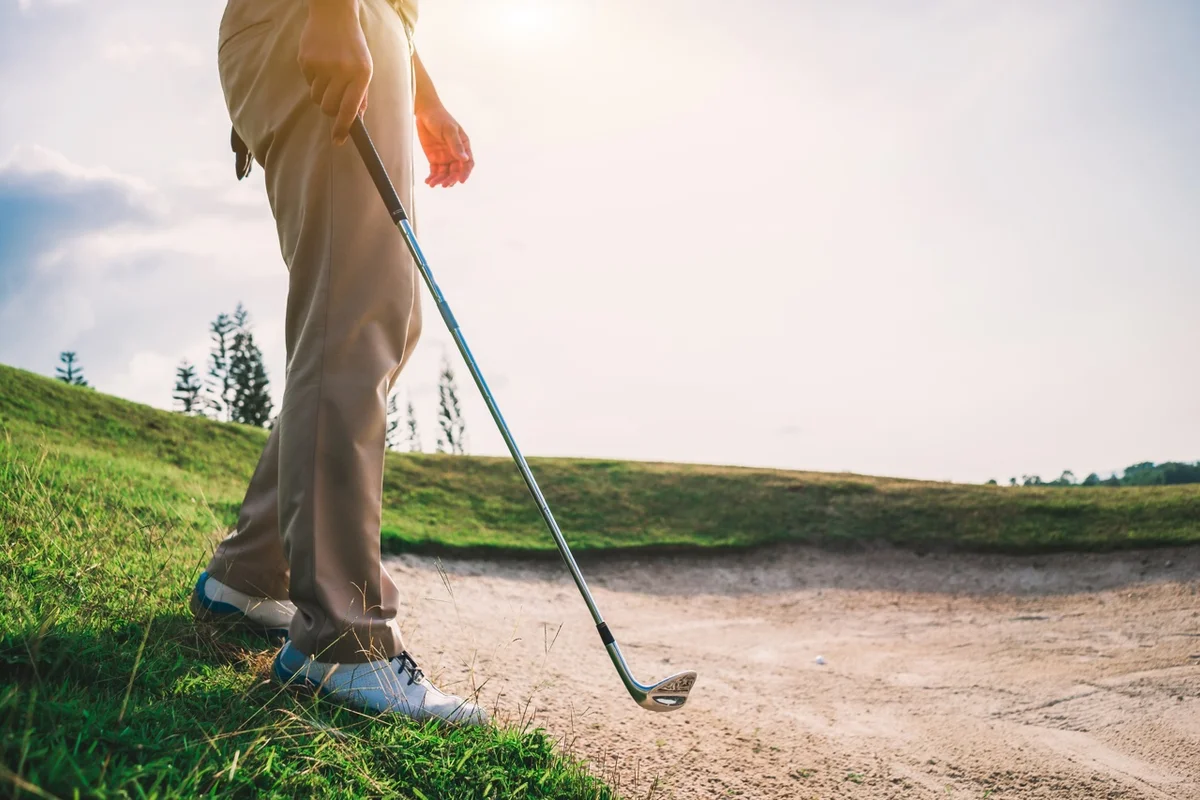 Golfer enters a bunker with a wedge
