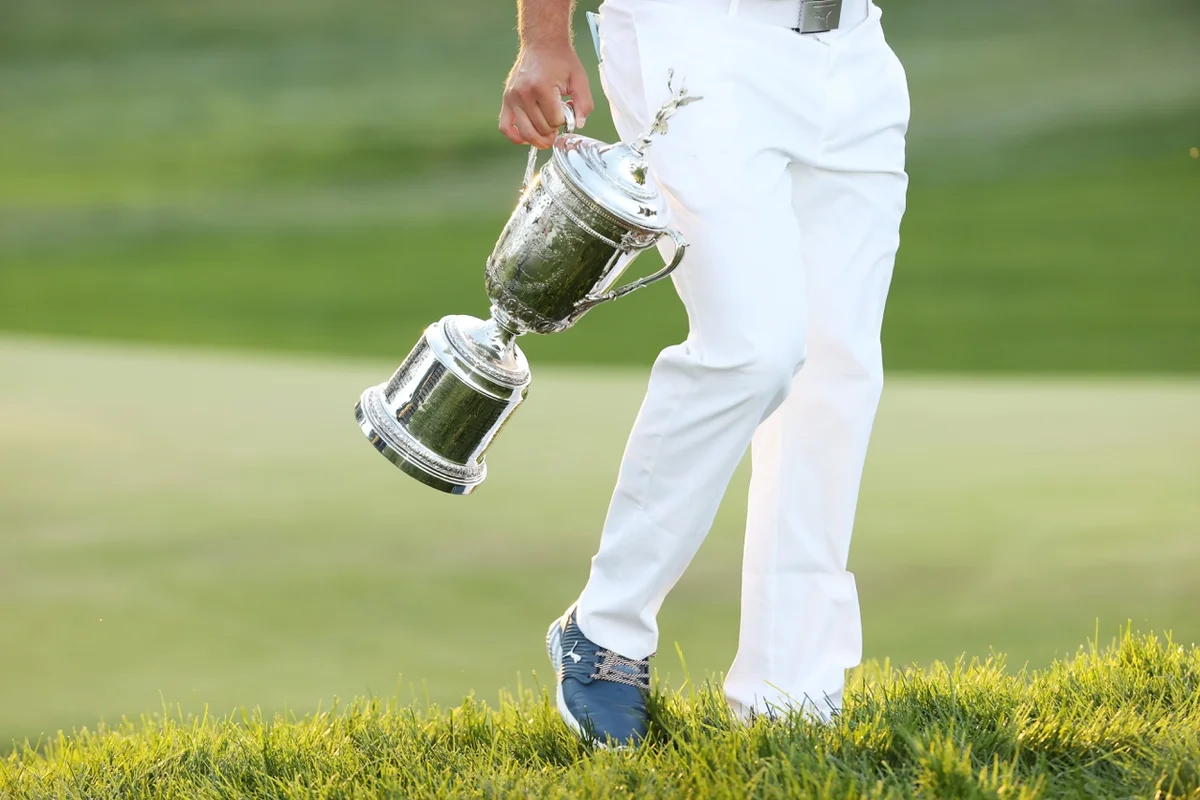 The U.S. Open trophy hangs by Bryson DeChambeau’s legs