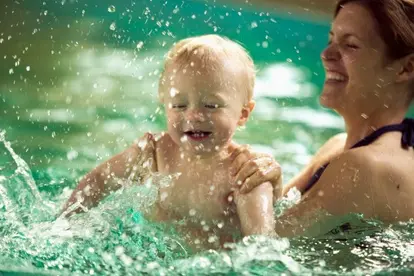 Mother splashing with baby son in swimming pool