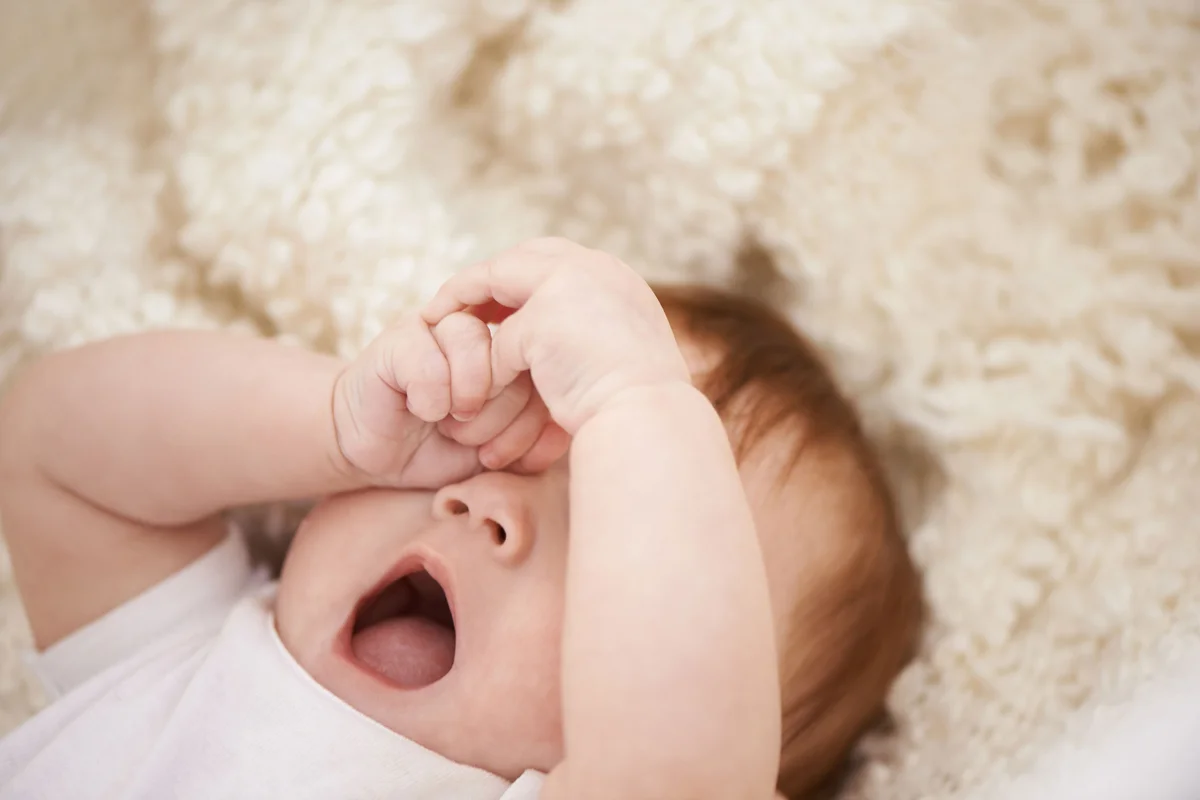 tired baby yawning and rubbing eyes