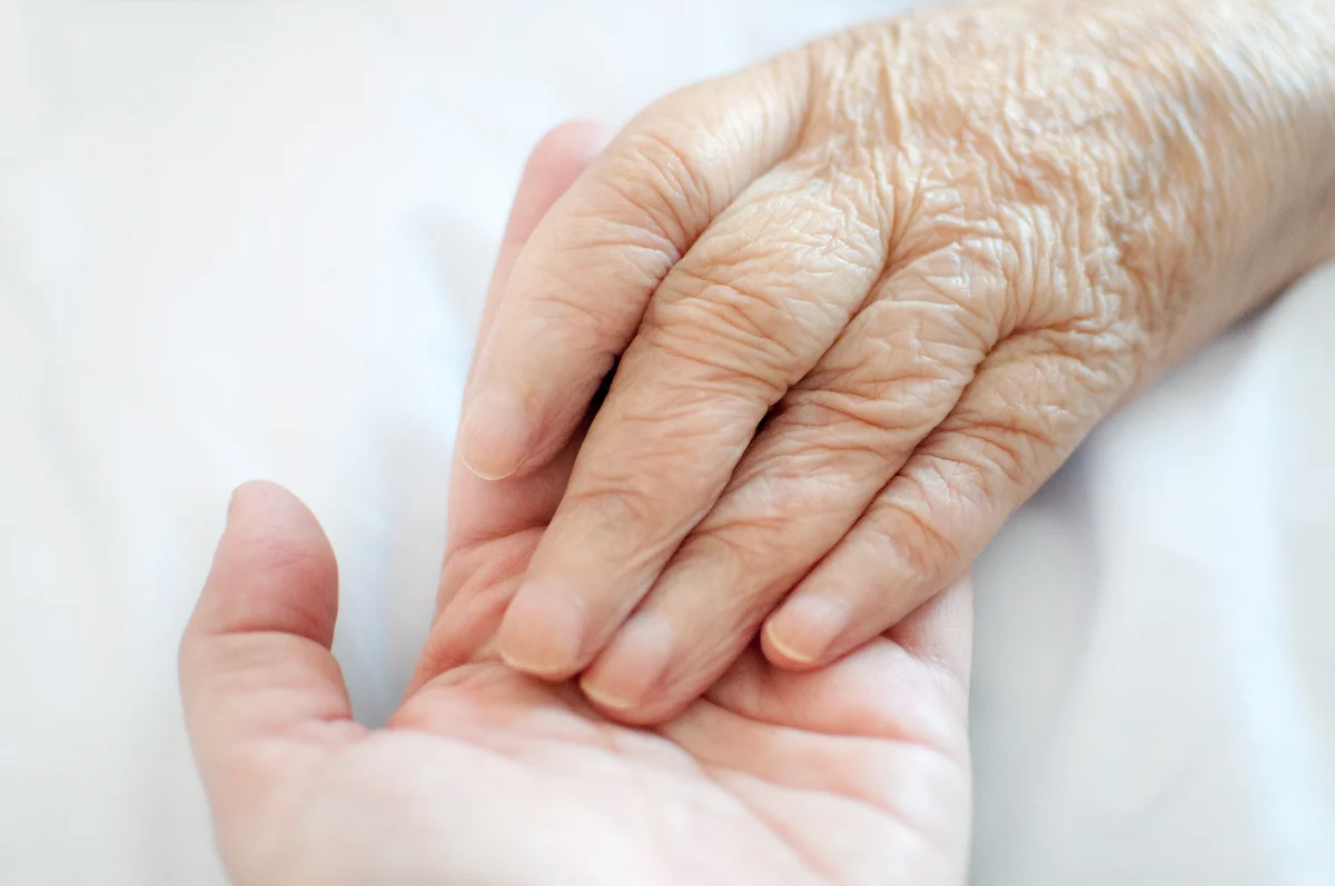 A young hand touches an old wrinkled hand