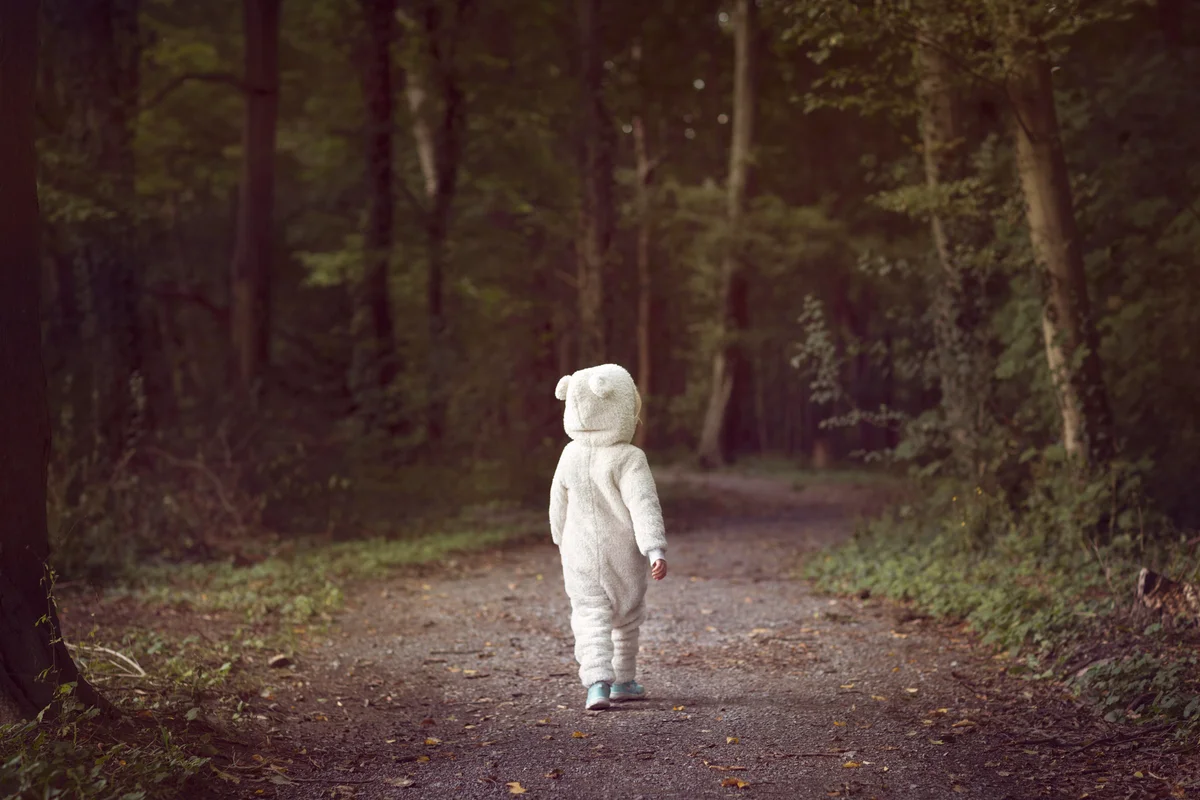 Small child wearing white bear suit in the woods