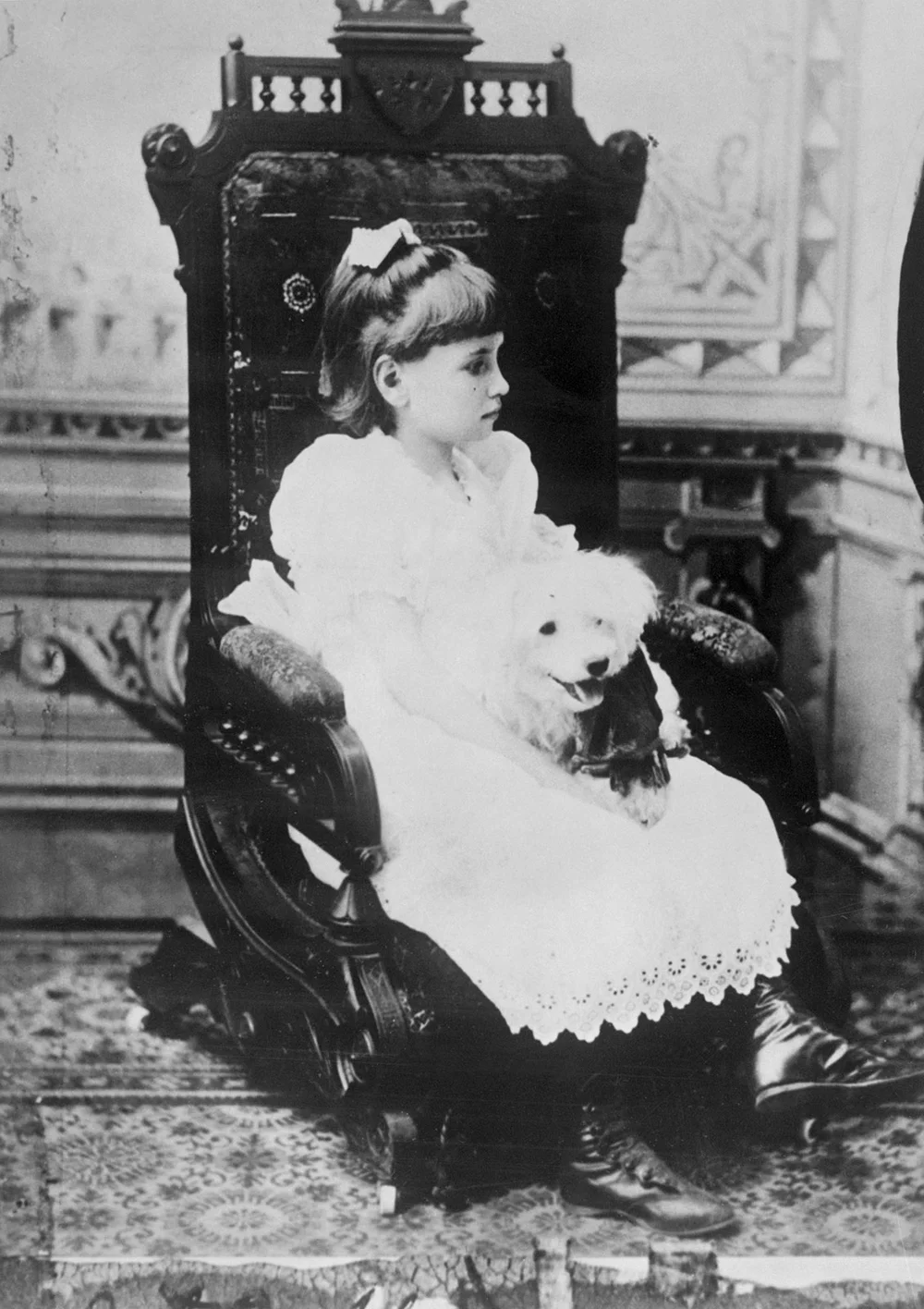 Young Helen Keller holding poodle in chair