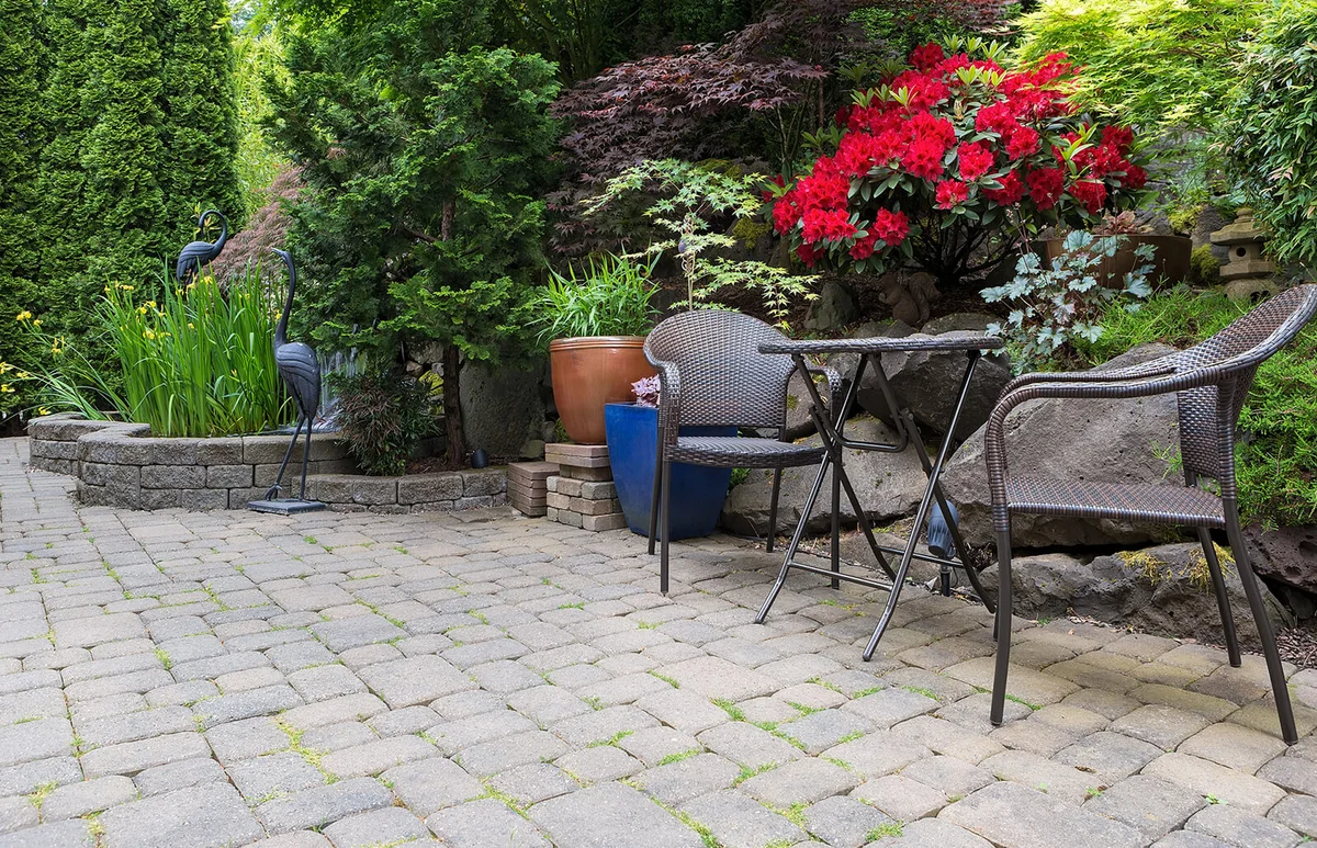 Garden backyard with lush plants landscaping pond water fountain and stone paver patio hardscape with wicker bistro furniture chair and table set