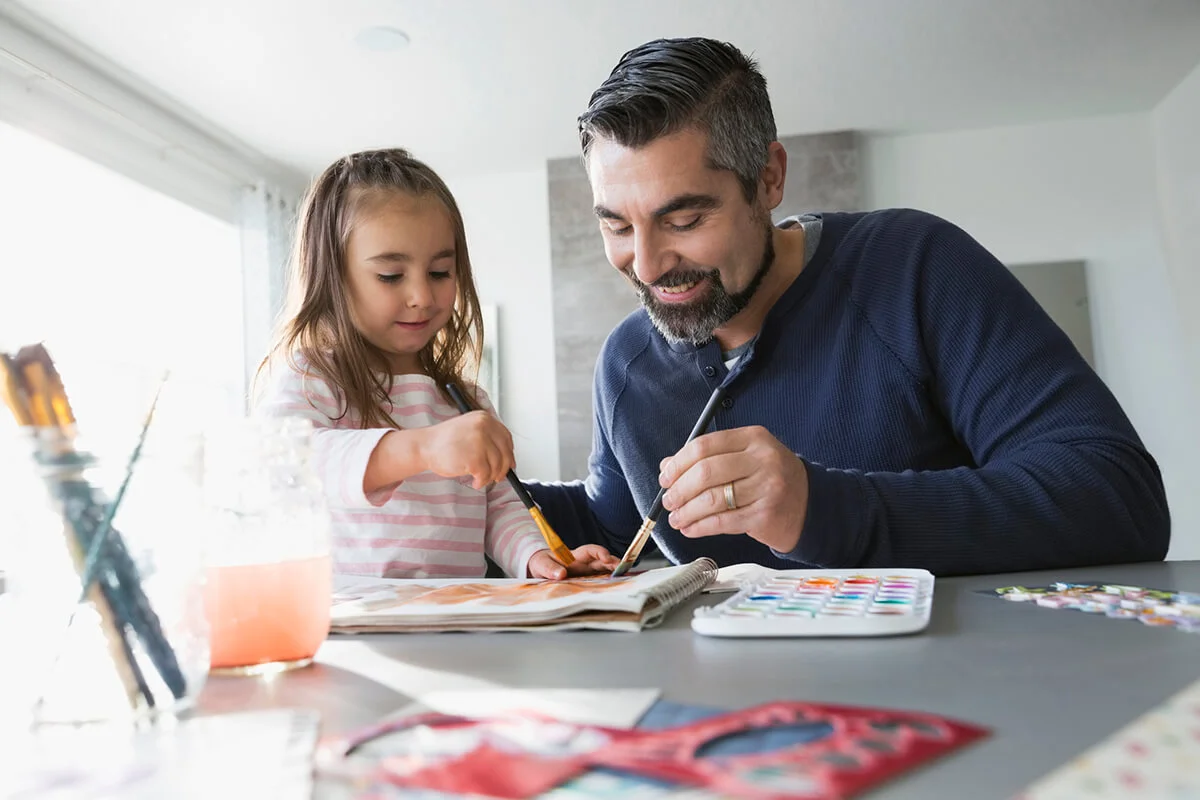 Father and daughter painting at dining room table