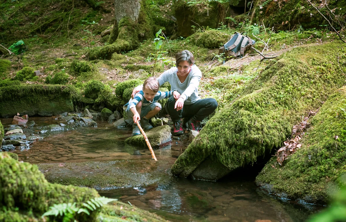 Mother and little son crouching at edge of a brook