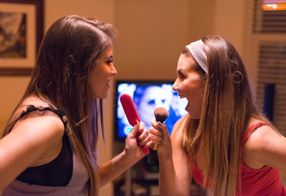 Two young women, singing into hair and make-up brushes