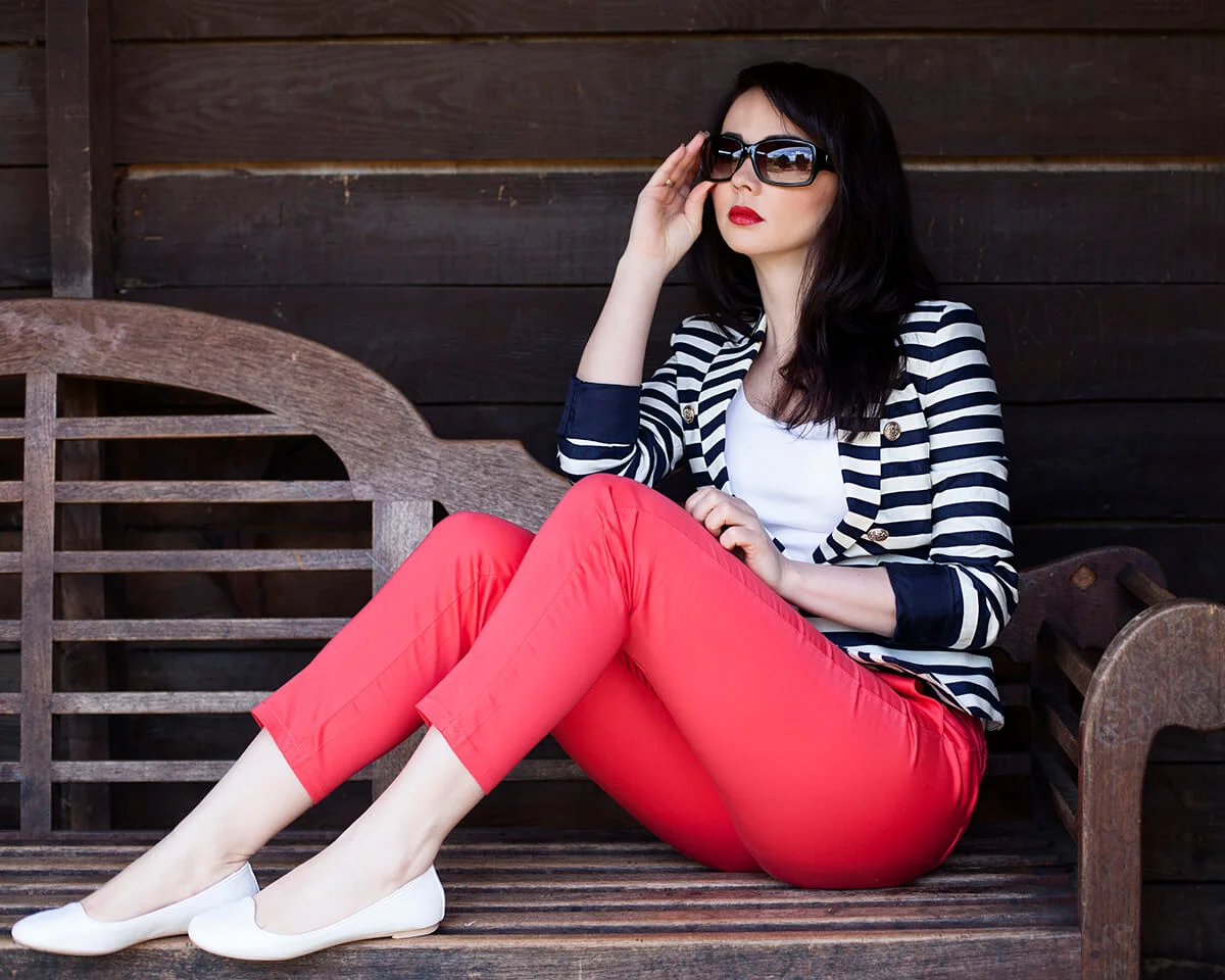 Young woman wearing striped jacket, white top, coral trousers and sunglasses