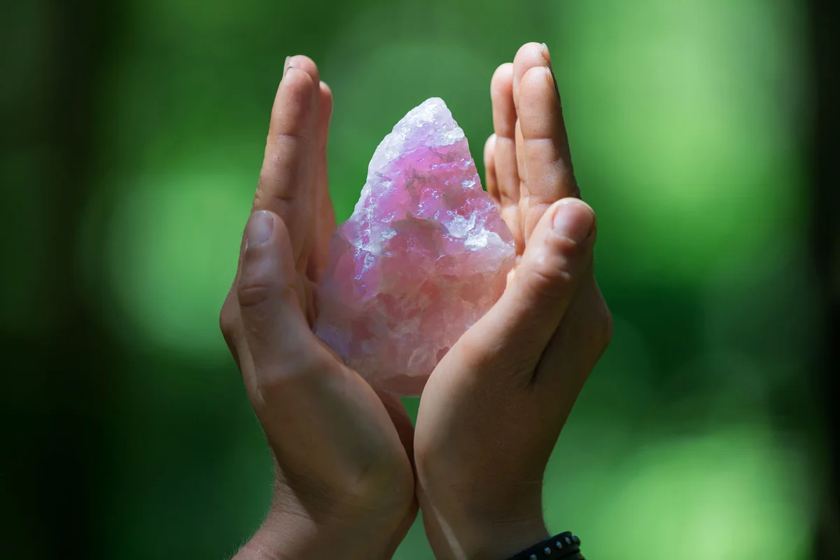 Hands holding a rose quartz crystal