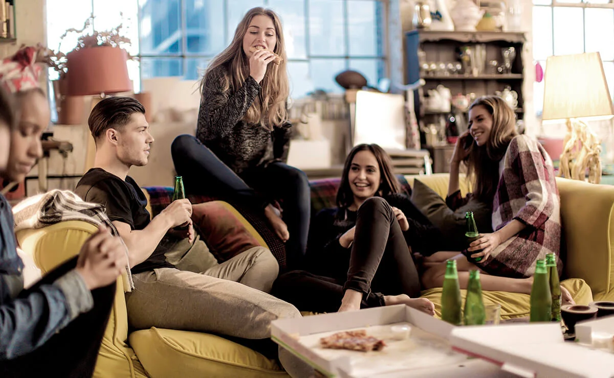 Friends sitting on a sofa, smiling, pizza and beer bottles on coffee table