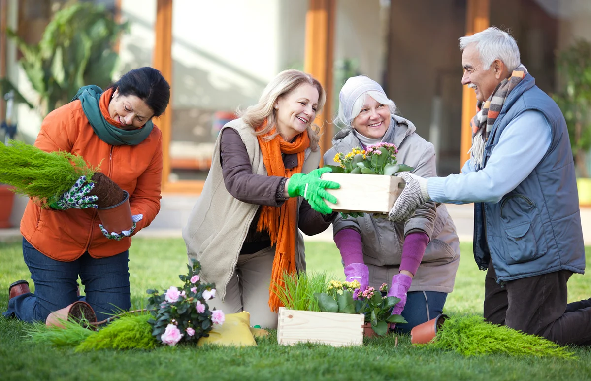 Senior friends gardening together in front of their retirement community house