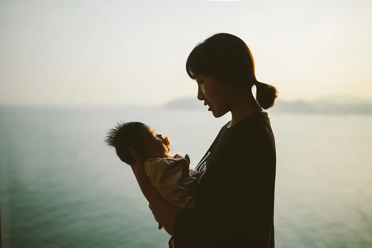 Mother hugging baby girl at home in front of window