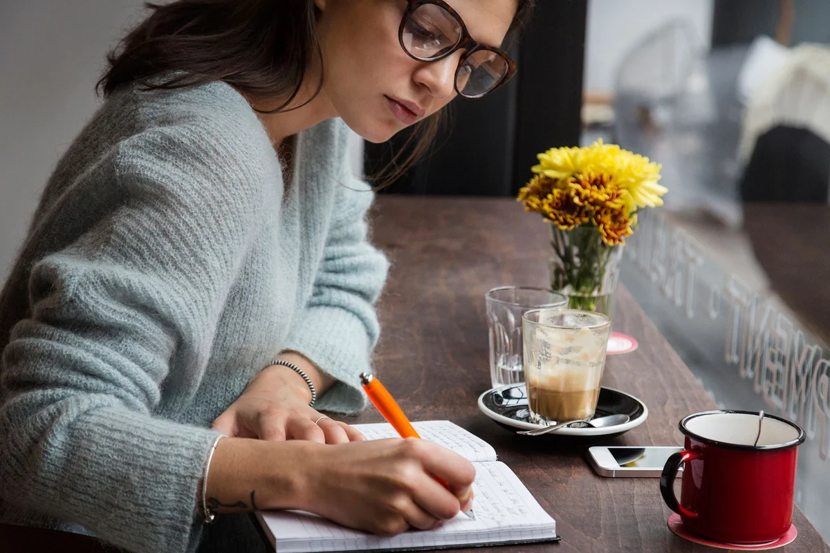 Woman writing in notebook in cafe