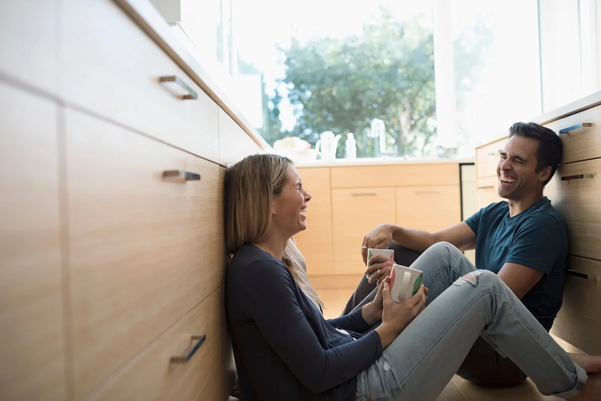 Happy couple laughing, drinking coffee on kitchen floor
