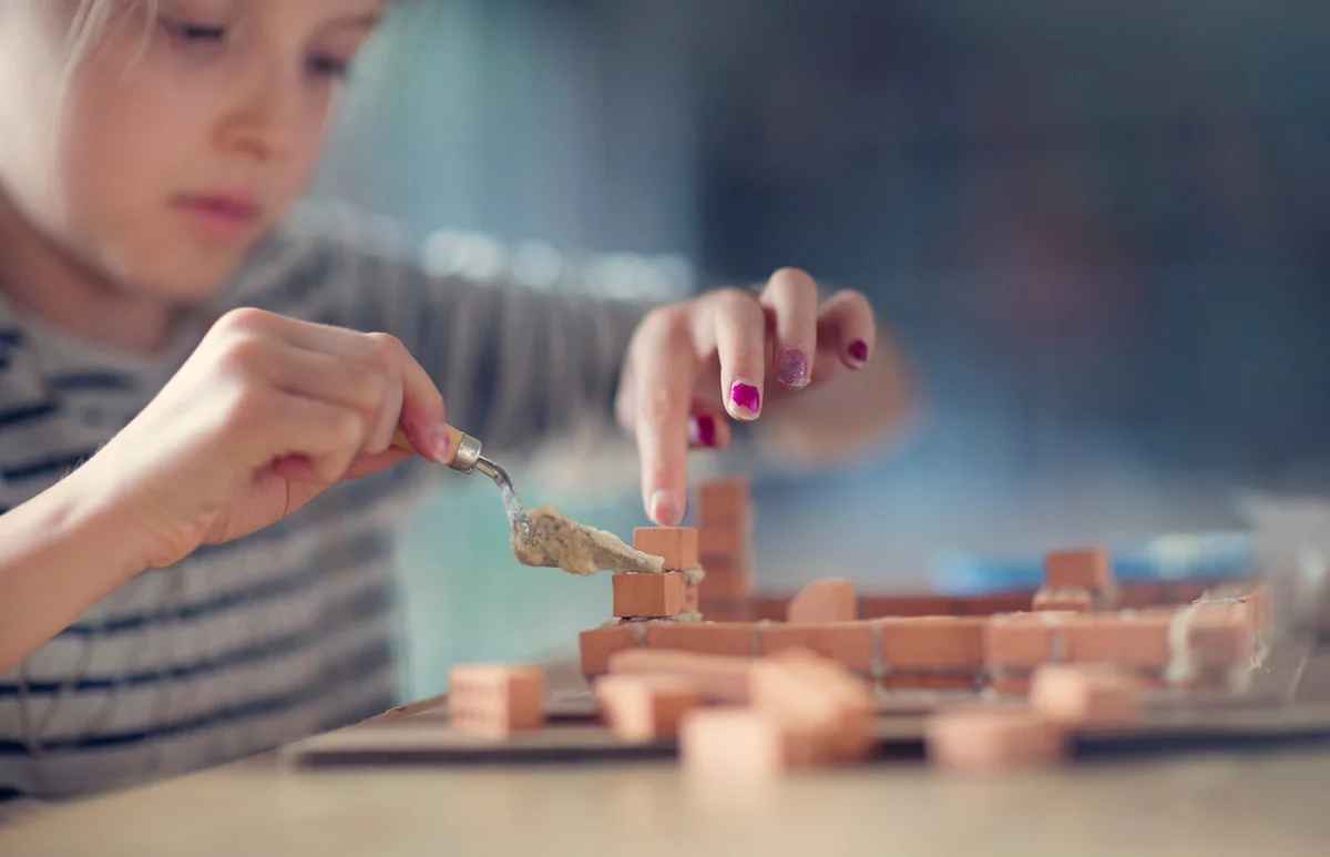 Girl building miniature house from bricks