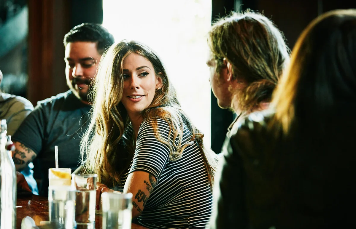 Smiling woman hanging out with friend while having drinks in bar