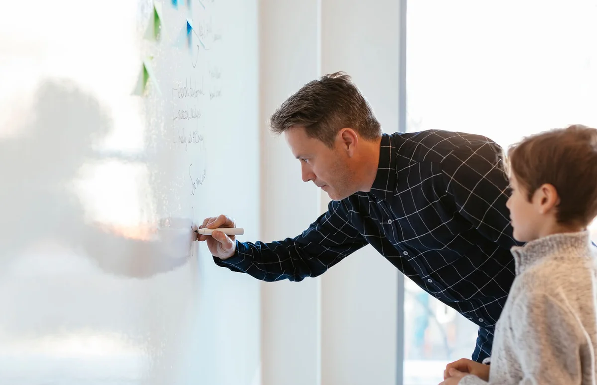 Businessman in office writing on whiteboard with son watching him
