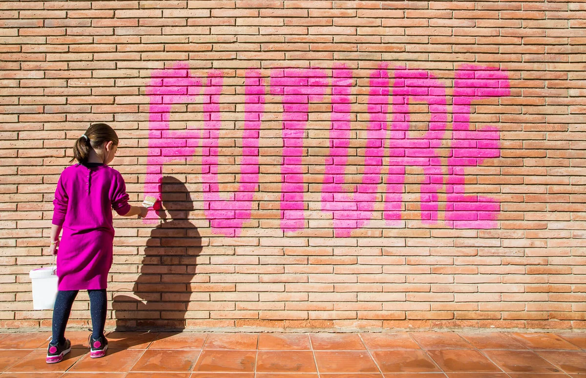 Little girl painting with pink colors the future word in a brick wall