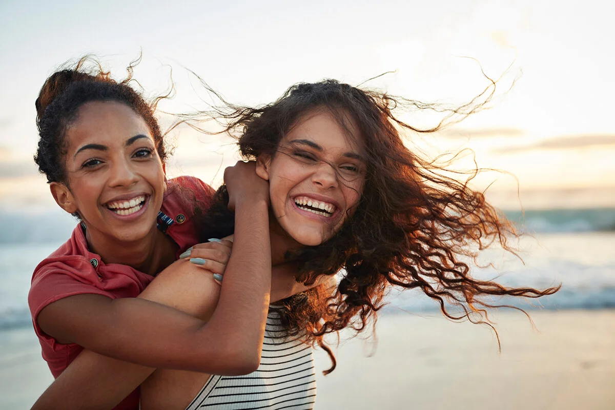 Young women piggybacking on sandy beach