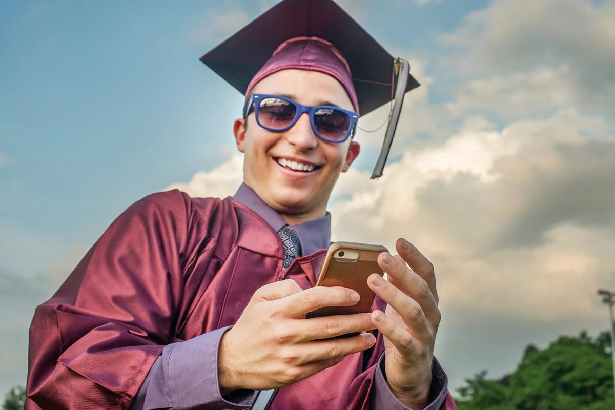 teen boy in cap and gown holding cell phone