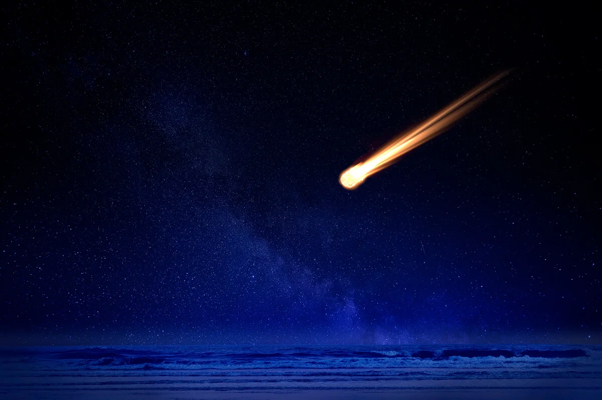 Meteor in night sky falling over ocean