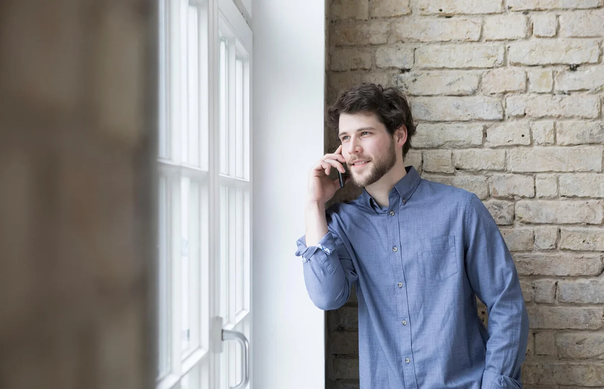 Young man talking on the phone by the window
