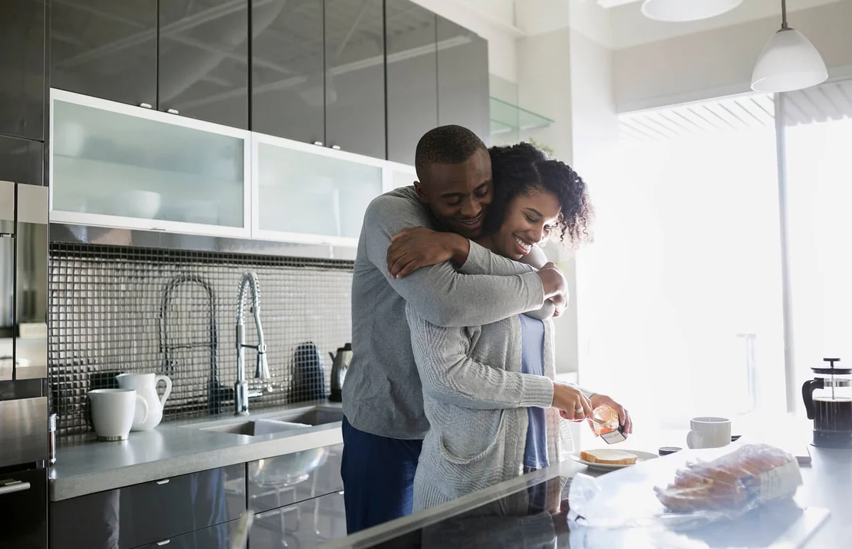 Smiling couple hugging and making breakfast in kitchen