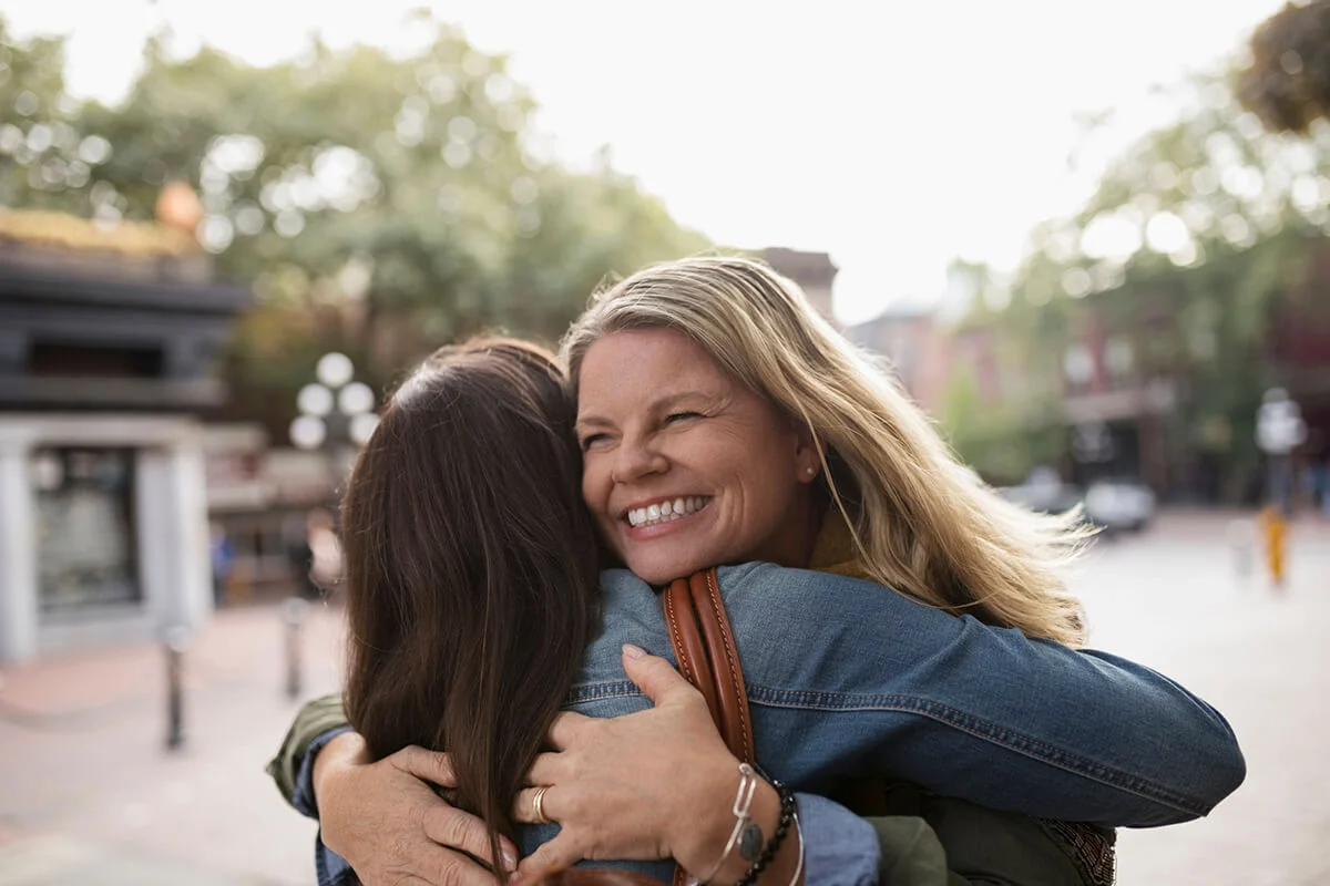 Enthusiastic mature women friends hugging on urban street