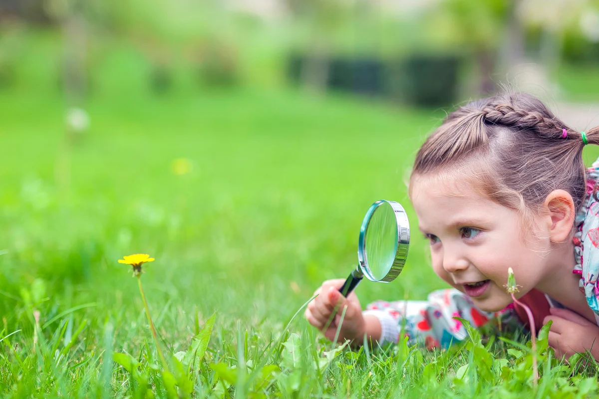 Girl with magnifying glass examining flower