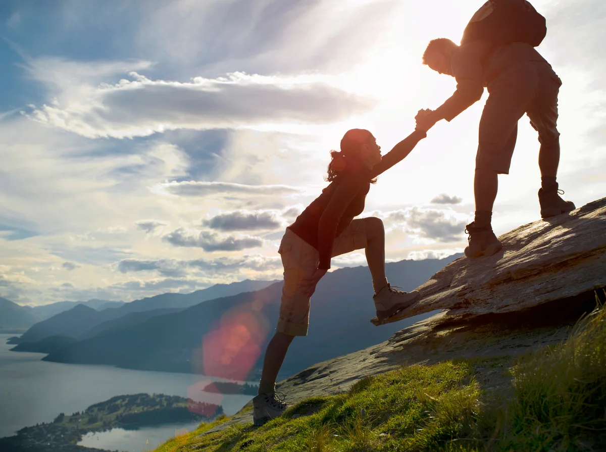 Silhouette of couple climbing hillside near a lake
