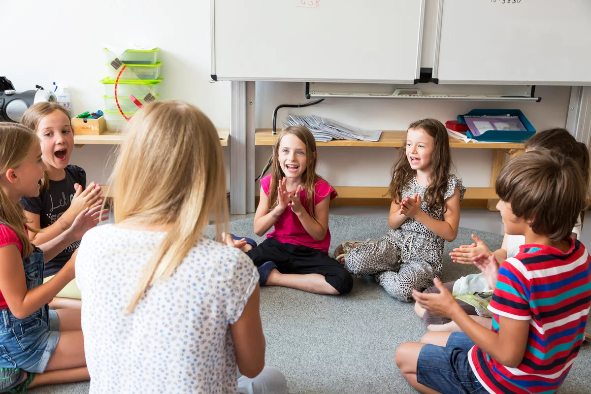 Teacher and pupils sitting on floor of their classroom