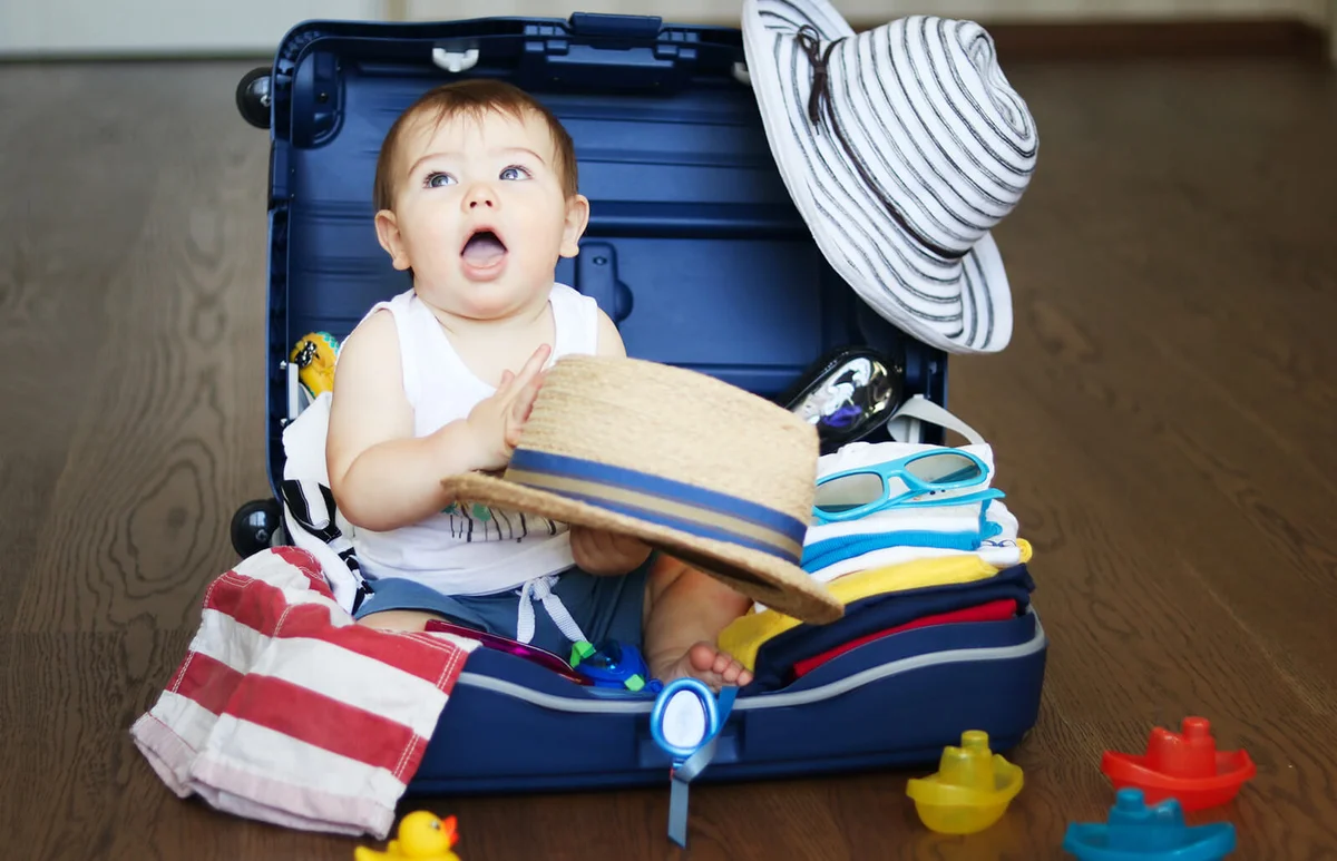 Cute baby boy sitting in the suitcase with hat in his hands