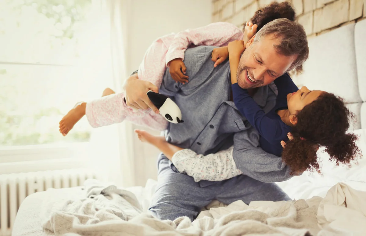 daughters playing and tackling father on bed