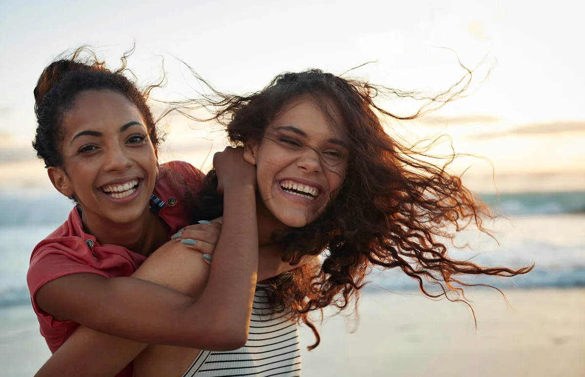 Young women piggybacking on sandy beach
