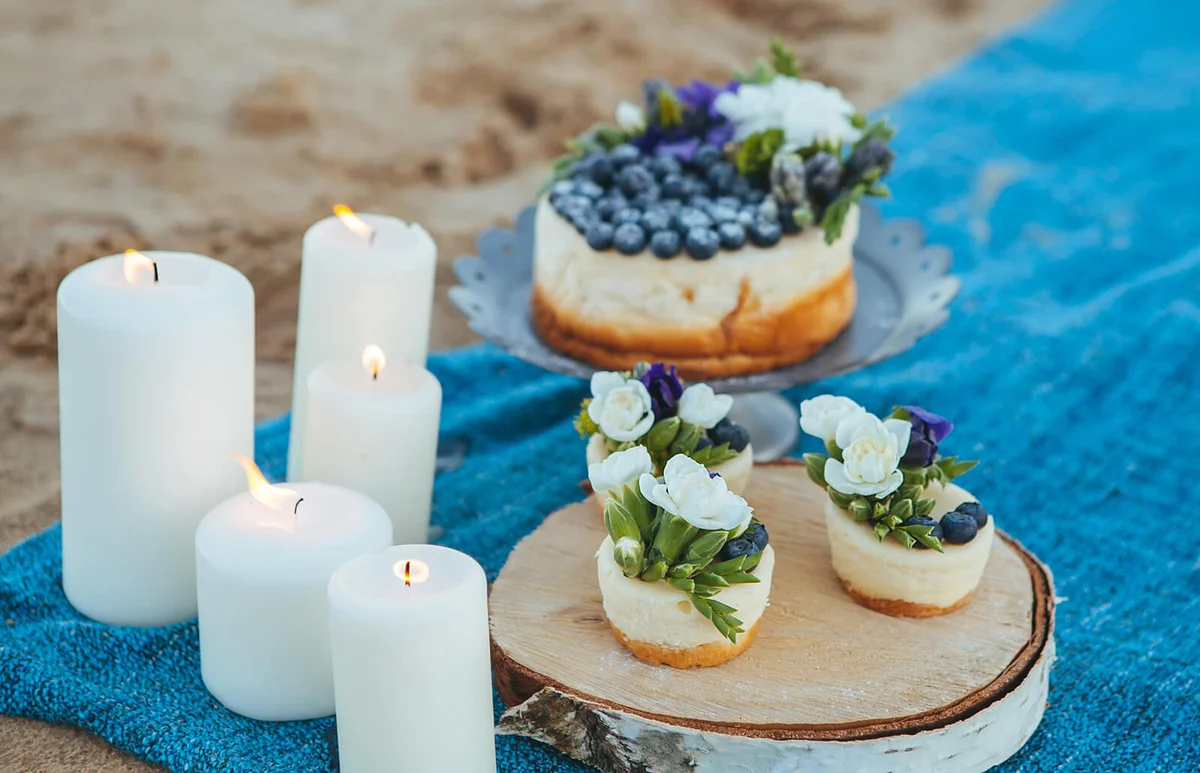 Cheesecake and capcakes decorated by blueberries and flowers on the sand / ID 93323545 © Kneyman | Dreamstime.com