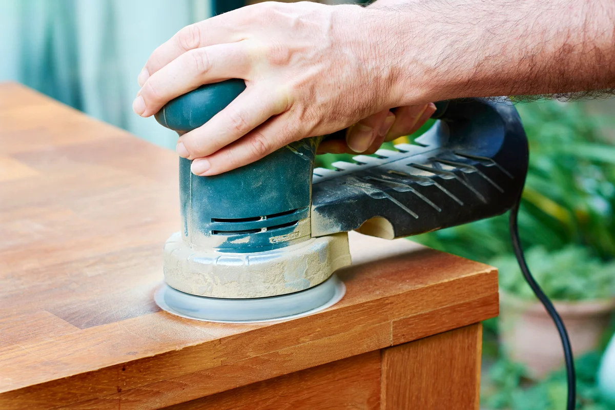 Man sanding an oak table with a random orbital sander