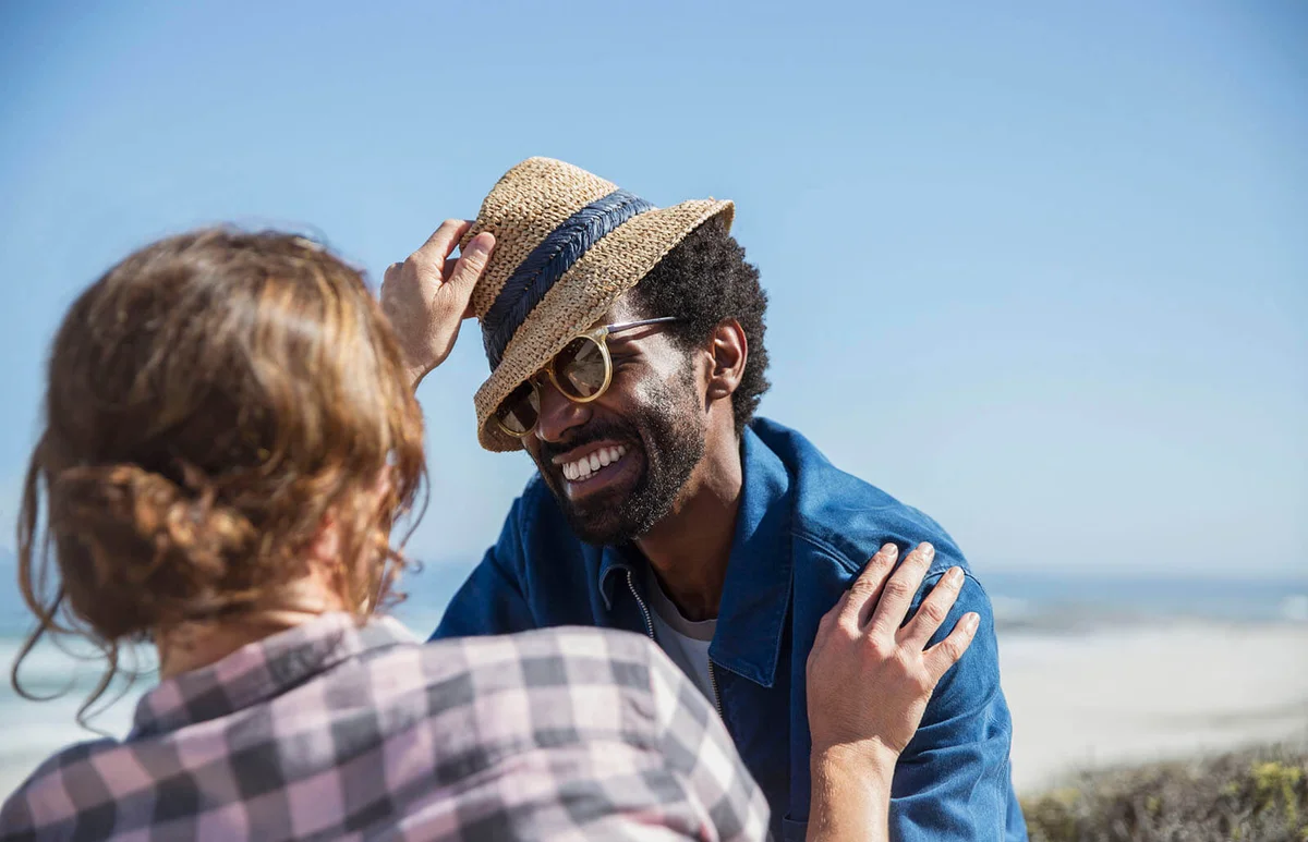 Playful couple with hat on sunny summer beach
