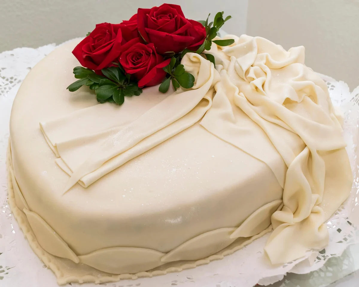 Wedding cake decorated in natural red roses and a ribbon made of icing sugar