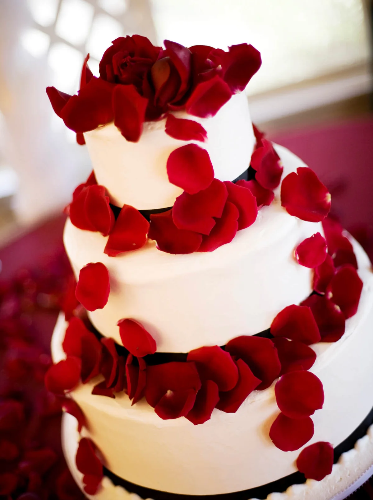 A layered wedding cake decorated with red rose petals