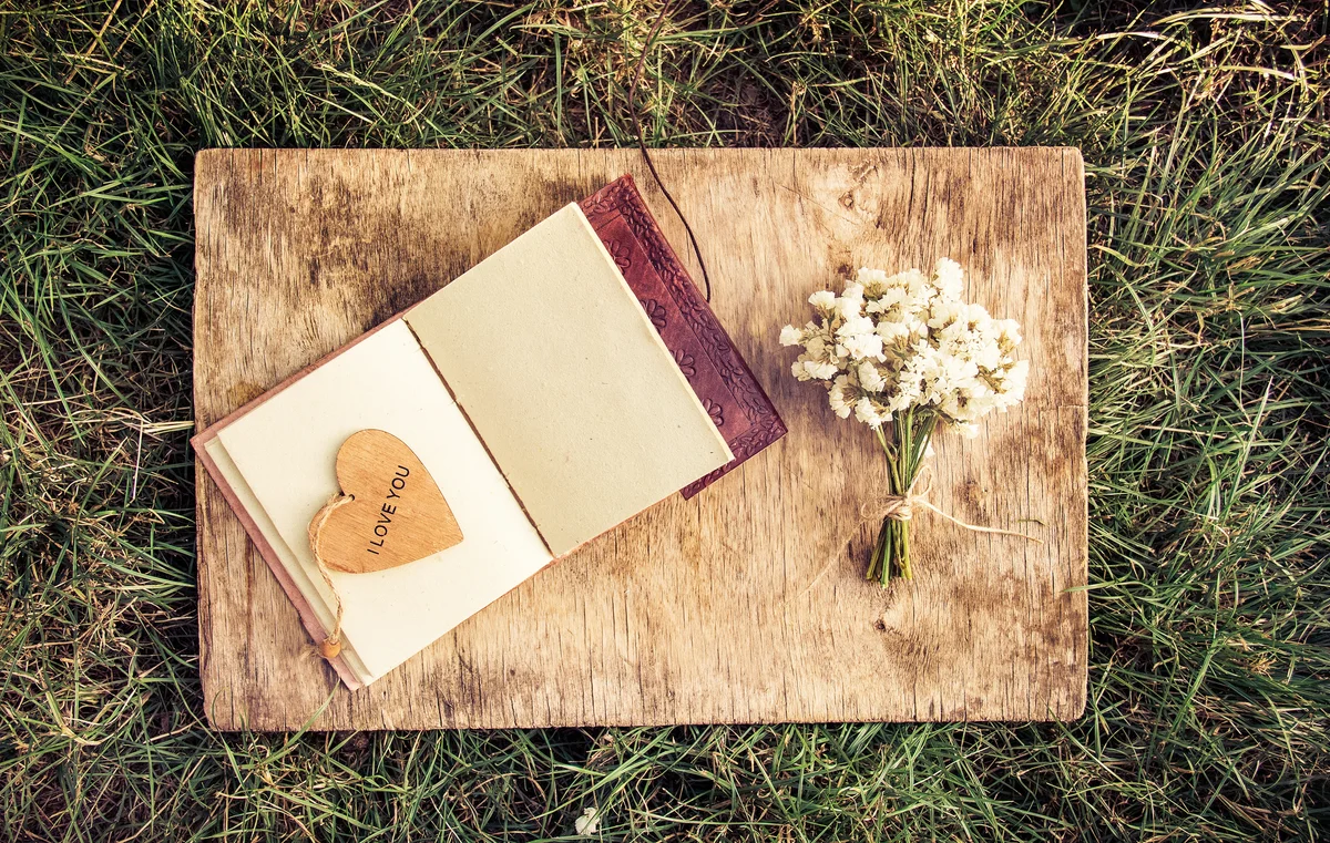 An open book with empty pages, a bouquet of white flowers and a wooden heart