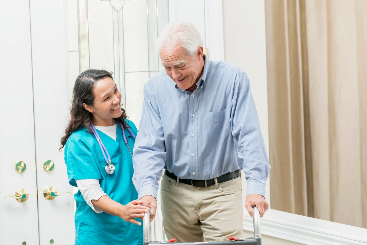 Home healthcare worker helping elderly man with walker