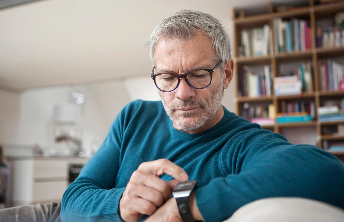 Man at home sitting on couch looking at watch