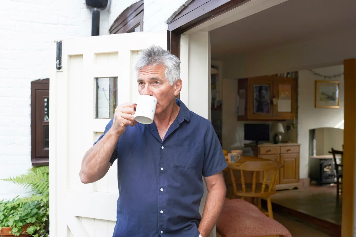 Mature man drinking tea in the doorway of his house