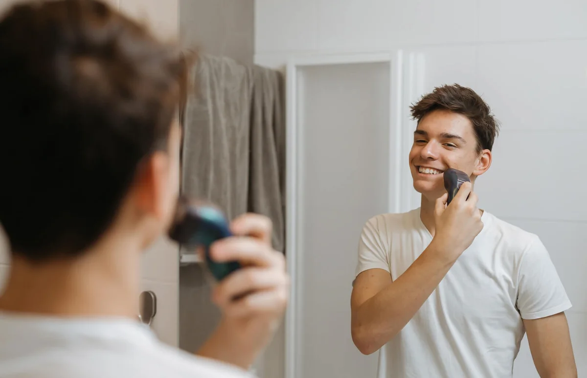 teenager shaving with electric razor in bathroom