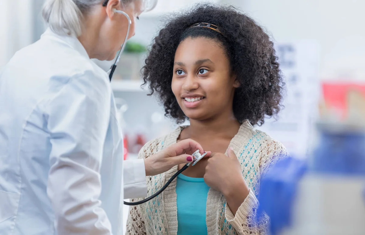 Physician listens to teenage patient's heart