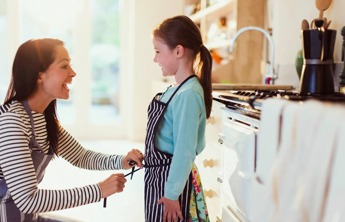 Mother tying apron on daughter in kitchen