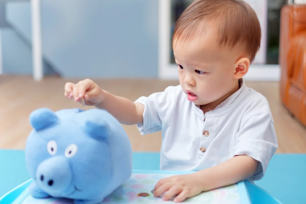 Toddler baby boy child putting coins into blue piggy bank