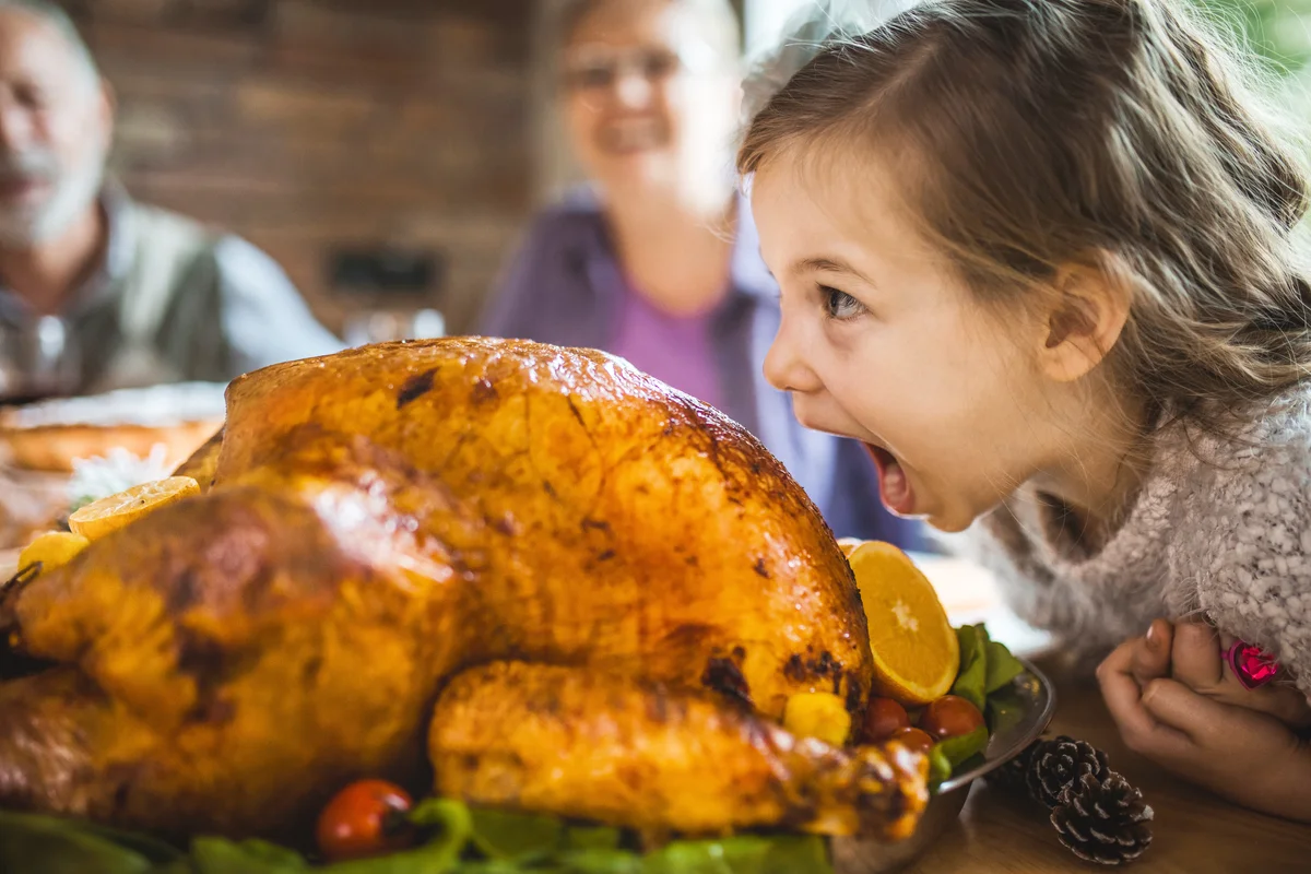 Cute little girl having fun while about to bite a stuffed turkey during Thanksgiving dinner in dining room