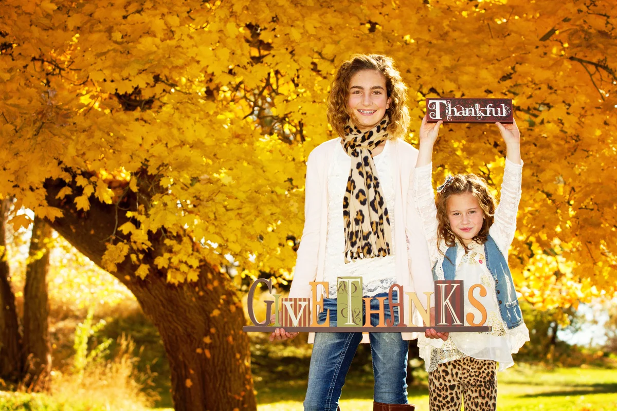 Sisters holding signs saying 'Giving Thanks' and 'Thankful' on a beautiful autumn day