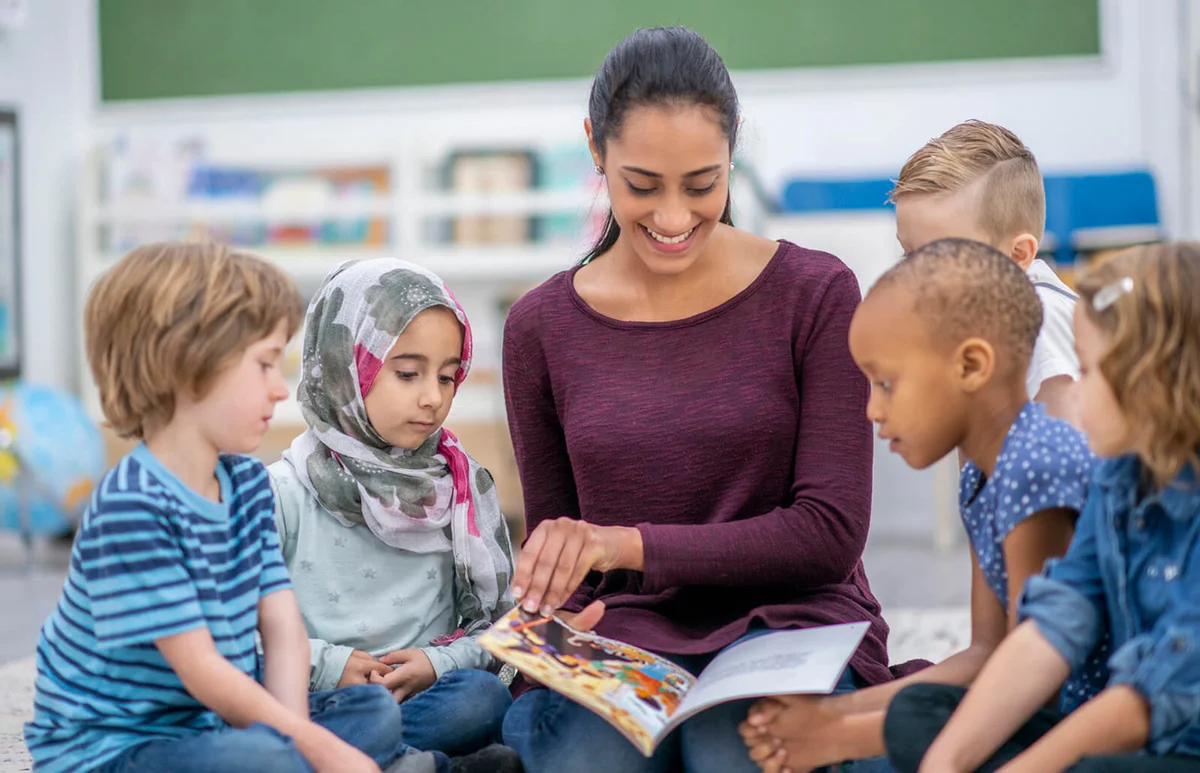 school children and teacher reading a book together